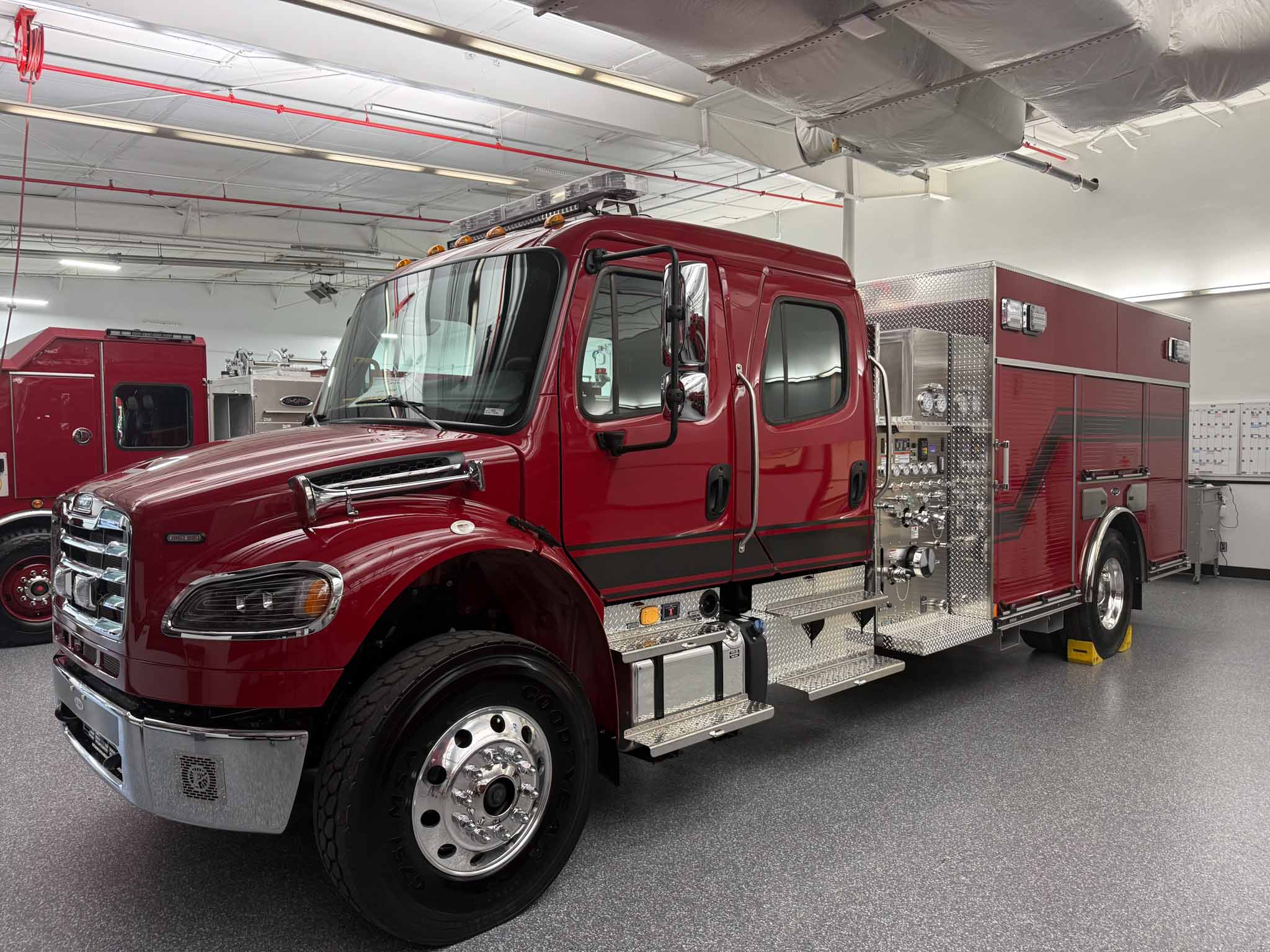 148884_frieghtliner rescue pumper-7 Red fire engine in a maintenance bay, showing chrome bumper, large tires, and equipment compartments on the side.
