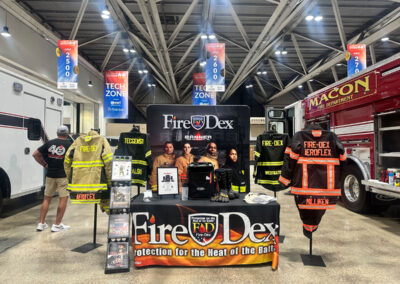 Fire-Dex trade show booth displaying firefighter turnout gear and a banner with 'Fire-Dex' branding, at a fire department expo.