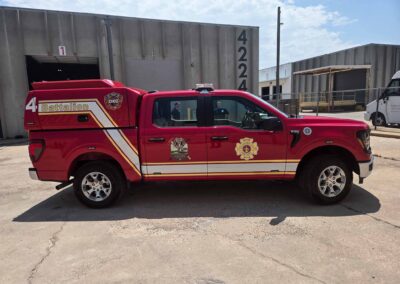 Red fire department pickup with '4 Battalion' markings parked in front of an industrial building, emergency logos visible on door