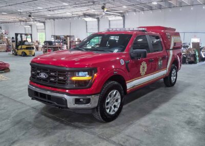 Red fire department utility pickup in a large workshop with a forklift, shelves, and boxes in the background.