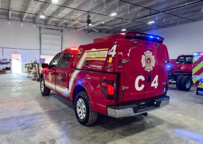 Red fire department rescue vehicle inside a garage, marked Battalion 4, with blue/red lights on top.