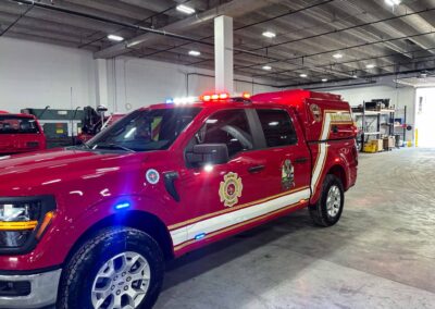 Red fire department rescue truck inside an industrial garage with flashing emergency lights on the cab roof and equipment in the background