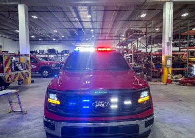 Front view of a Ford police SUV with red and blue emergency lights on in a warehouse, surrounded by shelves and equipment.",