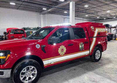 Red emergency response truck in a spacious indoor garage, with a light bar on the roof and department badges along the side.