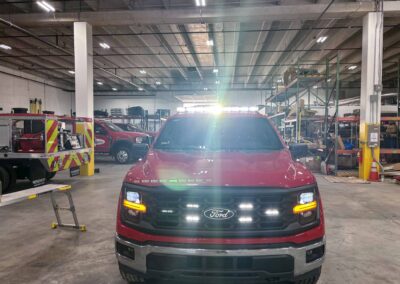 Red Ford pickup truck facing the camera inside a large industrial garage or warehouse, with equipment and shelving in the background and bright ceiling lights.