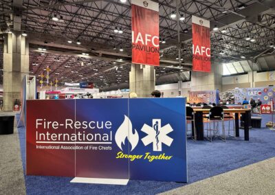 Large red IAFC Pavilion banners hang from the ceiling of a convention hall, with a Fire-Rescue International booth in the foreground.