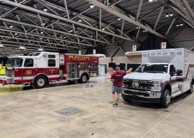 Indoor exhibit hall with fire trucks (Macon Fire Department) and a white rescue truck; a man in a maroon shirt stands near equipment in the foreground.