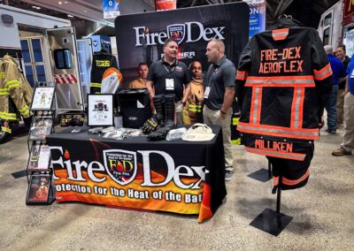 Fire-Dex booth at a trade show displaying firefighter PPE like jackets, gloves, and boots on a table and displays.