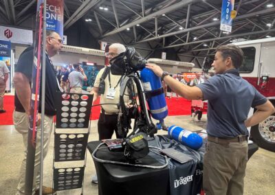 Man demonstrates scuba diving equipment at a trade show, with blue air cylinder attached to a harness and Dräger branding in view.