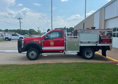 Red fire engine labeled Brush 2 from Pocola Fire Dept parked beside a metal-sided building under a blue sky with scattered clouds.