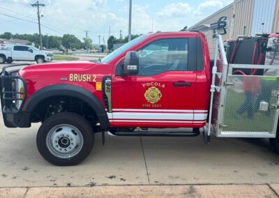 Side view of a red fire truck labeled BRUSH 2 with equipment rack and a diamond-plate utility area, Pocola Fire Dept. badge visible on door.