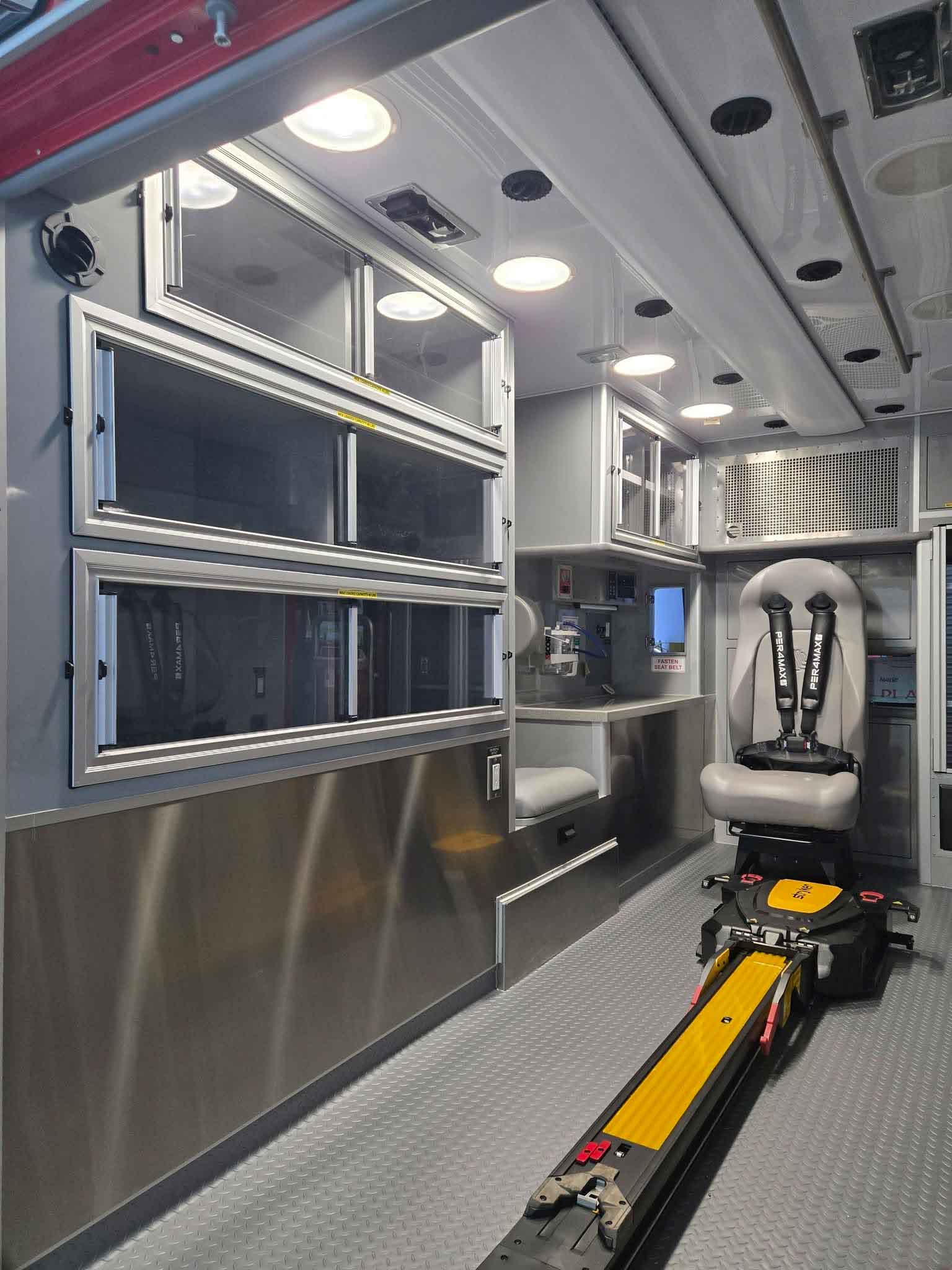 Rear and side view of a white emergency ambulance with red and black chevron stripes and multiple roof lights, parked on a street.